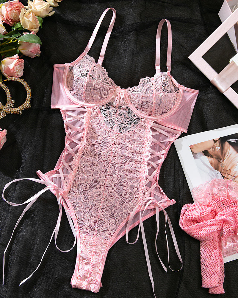 Pink lace lingerie set on a black surface with flowers and jewelry.