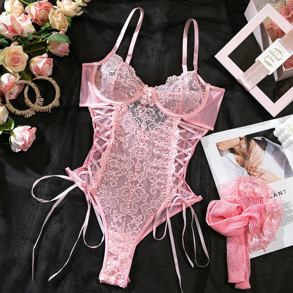 Pink lace lingerie set on a black surface with flowers and jewelry.