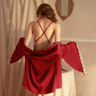 A woman wearing a red satin lingerie set with lace trim and a matching robe. The set includes a satin slip dress with sheer lace paneling, a flowing satin robe with wide sleeves, and a coordinating panty.