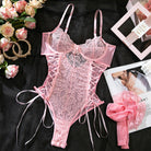 Pink lace lingerie set on a black surface with flowers and jewelry.